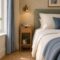 Slim wooden bedside cabinet with a drawer and open shelf beside a bed, beneath a wall-mounted reading light.